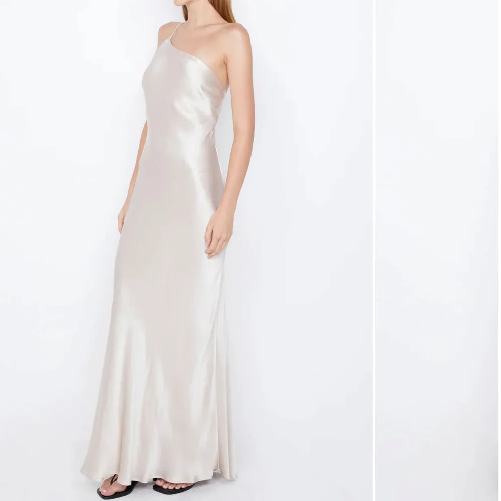 Elegant champagnefÀrgad lÄngklÀnning i satin med en stilren oneshoulder-design. KlÀnningen har en öppen rygg med smala band som korsas för en extra touch av glamour. Perfekt för bal!! AnvÀnd endast en gÄng. Mekot.