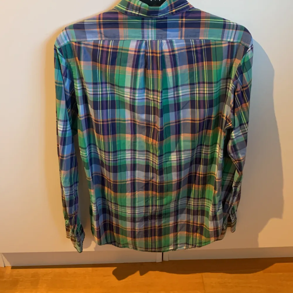 Säljer en färgglad rutig skjorta från Ralph Lauren i storlek S. Skjortan har långa ärmar och knappar framtill. Den är i en mix av gröna, blå och orange nyanser med ett broderat märke på bröstet.. Paidat.