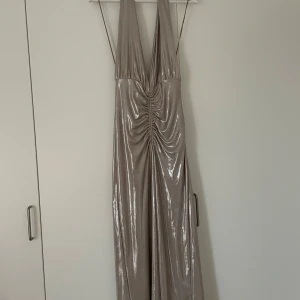 Skimrande långklänning från Zara - Säljer en skimrande långklänning från Zara i en elegant silverfärg. Går ned till ankeln och jag är 168cm lång. Klänningen har en djup v-ringning och är djup i ryggen. Den är perfekt för en glamorös kväll. Har aldrig fått användning för den men kanske du kan! 
