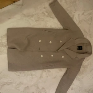 Zara Beige kappa med knappar - Elegant beige kappa med dubbelknäppning och klassisk krage. En tidlös favorit i garderoben. Köparen står för frakt.