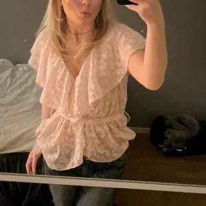 Rosa blus med volangdetaljer - Säljer en söt rosa blus med volangdetaljer och leopardmönster. Blusen har korta ärmar och ett knytband i midjan för en fin passform. Perfekt för en stilfull look.