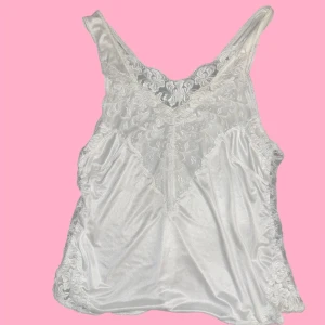 Vit spetslinne - Elegant vit linne med spetsdetaljer. Perfekt för en somrig look med vackra spetsmönster längs kanterna och axelbanden. Mjukt och bekvämt material som ger en lyxig känsla.