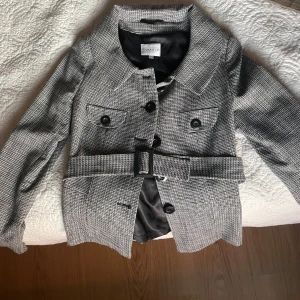 Kappa från Stockh LM - Snygg grå rutig kappa från Stockh LM med knappar och bälte i midjan. Väldigt old money vibe. nvänd endast ett par få tal gånger men är i nyskick. Inga fläckar eller slitage. Ny pris ca 1200kr säljer för 800 men pris kan diskuteras 🤍🤍