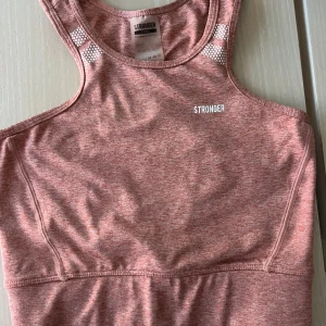 Rosa topp från Stronger - Säljer denna super snygga rosa toppen från Stronger. Toppen har ett sportigt utseende med breda axelband och ett diskret mönster vid axlarna. Perfekt för träning eller en aktiv dag!!😍