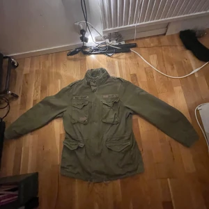 Grön m65 jacka från Brandit - Säljer en grön m65 jacka från Brandit i 100% bomull med polyesterfoder i ärmarna. Jackan har flera fickor framtill och en klassisk militärstil. Perfekt för en cool och avslappnad look.