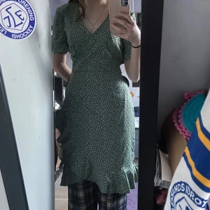 Grön prickig klänning från ONLY - Säljer en söt grön klänning från ONLY med små svarta prickar. Klänningen har en v-ringad design och korta ärmar med volangdetaljer. Den har en knytning i midjan och volangkant längst ner. Perfekt för en sommardag🌸 använd 1 gång så nästan ny, köpt från only för 350💞