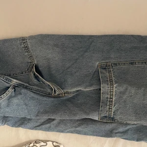 Blå jeans med slitna detaljer - Säljer ett par klassiska blå jeans med slitna detaljer och flera fickor. Perfekta för en avslappnad stil. De har en rak passform och är tillverkade i jeansmaterial. Cargo jeans 
