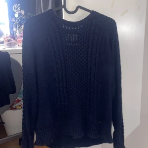 Mörkblå stickad tröja - Säljer en mysig mörkblå stickad tröja med flätstickat mönster. Tröjan har långa ärmar och en rund halsringning. Perfekt för kyliga dagar!