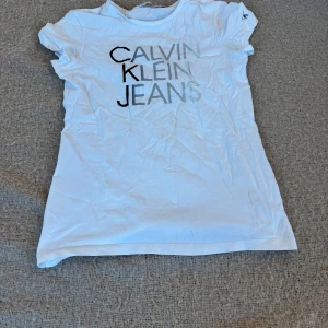 Vit t-shirt från Calvin Klein Jeans - Snygg vit t-shirt från Calvin Klein Jeans med tryck i svart. Perfekt för en avslappnad stil. Kortärmad och i en klassisk passform.