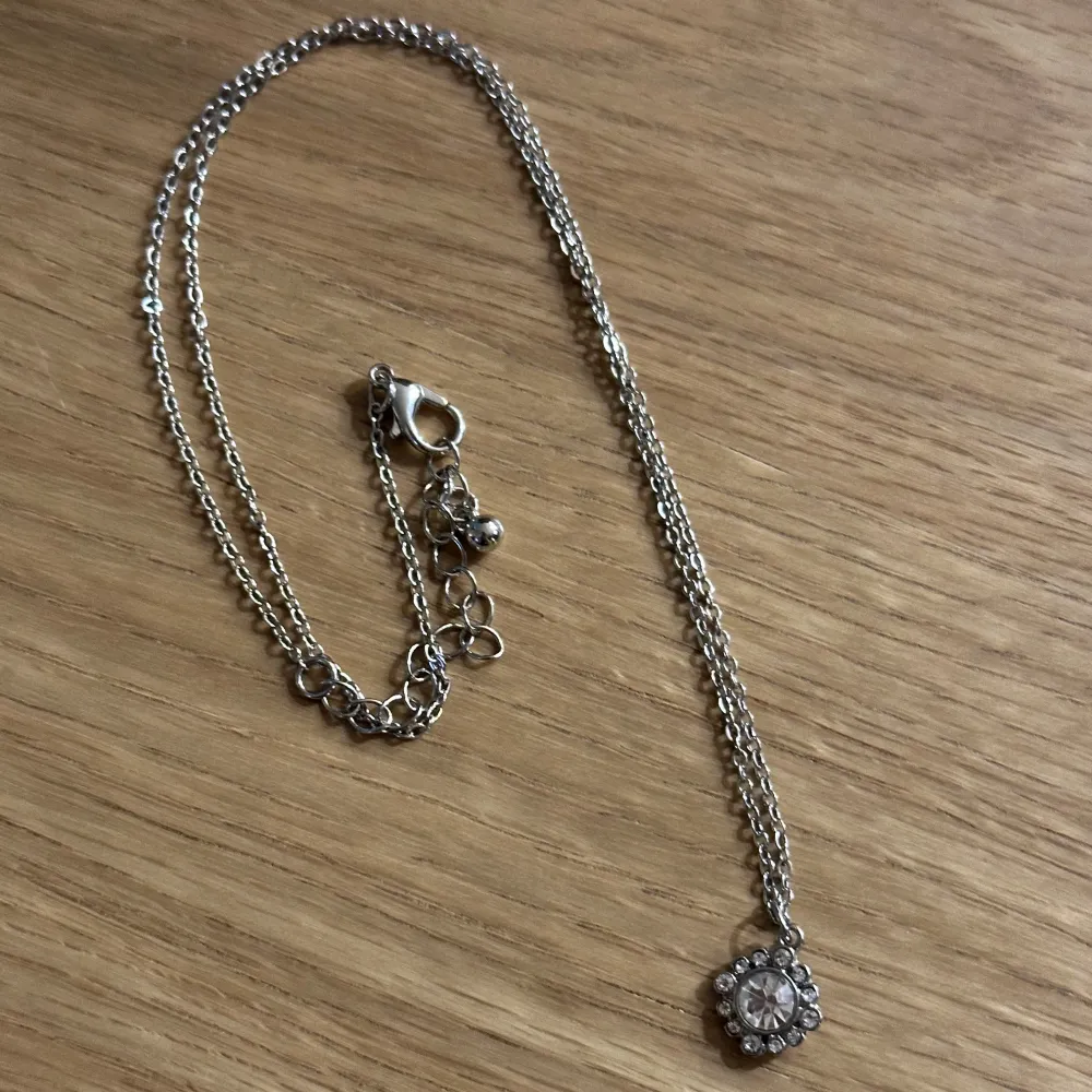 Elegant silverhalsband med ett hängsmycke i form av en blomma med fina stenar. Justerbar kedja med karbinhake för enkel användning. Oanvänd! . Asusteet.