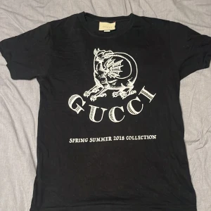 Svart Gucci t-shirt  - Snygg svart t-shirt från Gucci med ett coolt draktryck och texten 'Spring Summer 2018 Collection' på framsidan. Perfekt för dig som vill ha en stilren och trendig look.