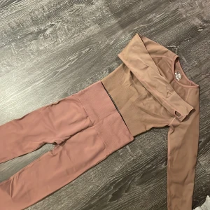 Brun set med topp och byxor - Säljer ett snyggt brunt set med en långärmad topp och matchande byxor. Setet är tillverkat av 90% nylon och 10% spandex, vilket ger en skön och stretchig passform. Perfekt för en avslappnad dag eller träning. I kameran ser det ut som att det inte är samma färg men det är samma färg!!!!!!!! Storleken är i M men passar även på XS och XSS