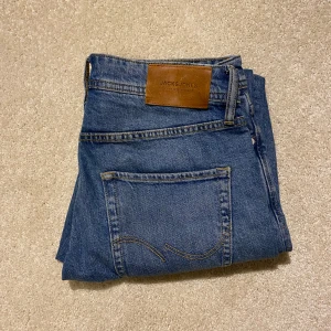 Blå jeans från Jack & Jones - Säljer ett par snygga blå jeans från Jack & Jones, modell Tapered/Mike. De har en klassisk femficksdesign och en bekväm passform med dragkedja och knapp. Perfekta för en avslappnad stil. Priset kan diskuteras
