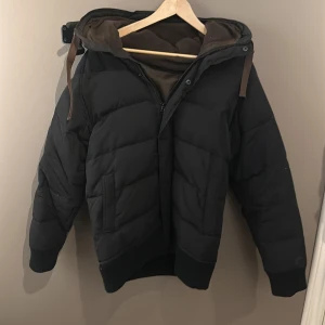 Svart pufferjacka från Vailent - Snygg svart pufferjacka från Vailent med huva och dragkedja. Perfekt för kyliga dagar med sin vadderade design. Jackan har långa ärmar och en stilren look.