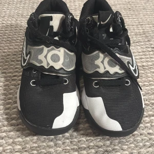 Svarta Kevin Durant sneakers från Nike - Snygga svarta Kevin Durant sneakers från Nike med vita och grå detaljer. Skorna har en unik sula med gul och vit mönstring och snörning för perfekt passform. Perfekta för basketentusiaster.  Med ny pris 1199 Kr 