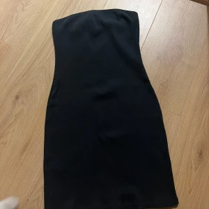 Svart axelbandslös klänning från MNG - Snygg svart axelbandslös klänning från MNG i en tight passform. Perfekt för en stilren look. Klänningen är ribbad och har en kort längd som ger en modern känsla.