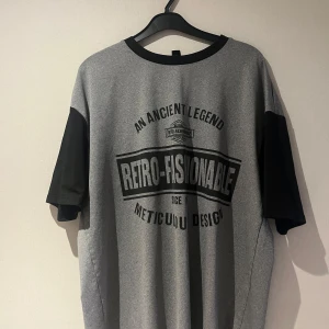 Grå och svart t-shirt med tryck - Snygg grå t-shirt med svart text och detaljer. Texten 'Retro-Fashionable' pryder framsidan. T-shirten har korta svarta ärmar och en rund halsringning.