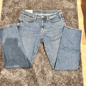 Blå H&M jeans - Säljer ett par klassiska blå jeans från H&M i regular fit. De har en rak passform med fem fickor och knappgylf. Perfekta för en avslappnad stil.