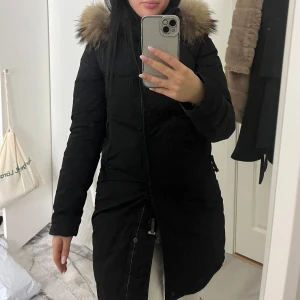 Parajumper - Snygg svart parkajacka från PJS med en mysig pälsdetalj på huvan. Jackan har en praktisk dragkedja och knappar framtill. Perfekt för kalla dagar. Dragkedjan är sönder men går att knäppa. Storlek xxs men som en xs 