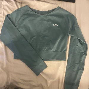 Grön croppad tröja från ICANIWILL - Säljer en snygg grön croppad tröja från ICANIWILL. Tröjan har långa ärmar och en stilren design med logga på bröstet. Perfekt för träning eller en avslappnad look.