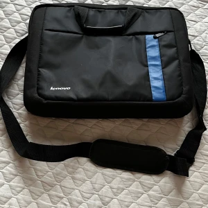 Svart datorväska från Lenovo - Snygg och praktisk svart datorväska från Lenovo med en blå detalj och dragkedja. Väskan har en axelrem och handtag för enkel transport. Perfekt för att skydda din laptop på språng.