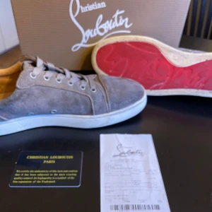 Grå sneakers från Christian Louboutin - Snygga grå sneakers i mocka från Christian Louboutin med den ikoniska röda sulan. Skorna har snörning och en stilren design som passar perfekt för en trendig look. Priset kan diskuteras vid snabb affär!