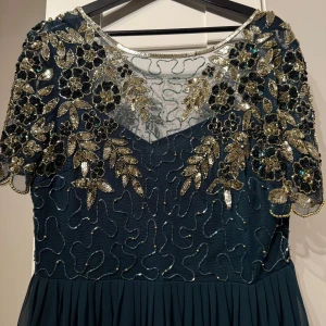 Festklänning - ASOS - En mycket fin och elegant lång festklänning i mörkgrön färg, köpt på ASOS. Klänningen är i väldigt bra skick och har endast använts tre gånger på bröllop. Den har inga defekter och har väldigt fina detaljer, samt är ungefär V-ringad på ryggen. Jag rekommenderar den starkt till bröllop eller andra fester, då den är väldigt fin💓