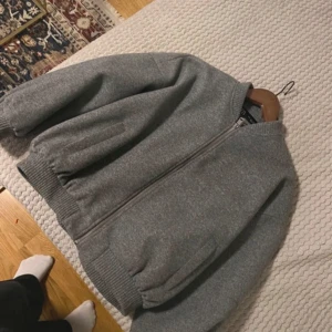 Grå bomberjacka - Snygg grå bomberjacka med dragkedja och ribbade muddar. Perfekt för en stilren look och passar bra till både vardag och utekvällar.