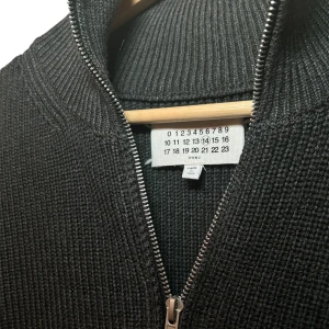Maison Margiela Full-zip L - Snygg svart/mörkgrå kofta från Maison Margiela med dragkedja och ribbad struktur. Perfekt för en stilren look. Den har en diskret design med märkets signaturstygn på baksidan. Storlek 48/L. Helt ny med lappen kvar 