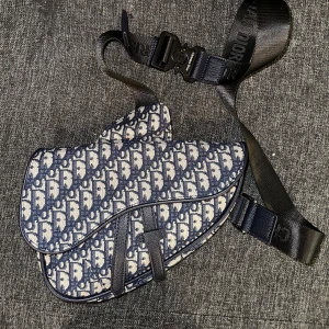 Mönstrad axelväska från Christian Dior - Snygg axelväska från Christian Dior med ett ikoniskt mönster i blått och vitt. Väskan har en justerbar rem med märkets logga och en säker spänne. Perfekt för att ge din outfit en lyxig touch.