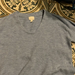 Grå v-ringad tröja - Säljer en stilren grå tröja med v-ringning. Tröjan har långa ärmar och är tillverkad i ett mjukt material som ger en bekväm passform. Perfekt för en avslappnad look.