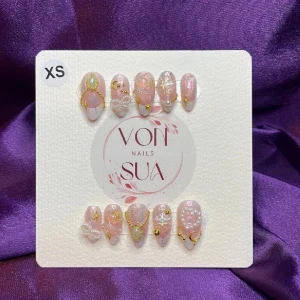 Glacia (XS); Medium Almond - Snygga rosa lösnaglar med glittrande detaljer och guldfärgade dekorationer. Perfekt för en glamorös look. Naglarna är i storlek XS och kan enkelt anpassas efter din nagelbredd.