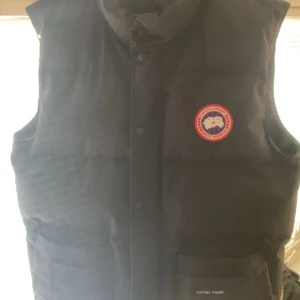 Canada goose väst - Säljer en svart canada goose väst i mycket bra skick. Storlek L. Riktigt snygg och Perfekt för kyliga dagar. Nypris ca 5000kr