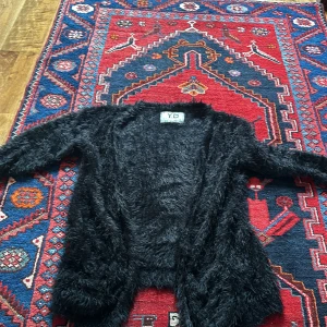 Svart fluffig kofta från Y.D - Säljer en supermjuk och fluffig svart kofta från Y.D. Perfekt för att mysa till det under kyliga dagar. Koftan har en öppen design utan knappar och är riktigt skön att ha på sig. Passar perfekt till både vardag och fest!