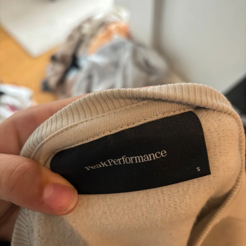 Säljer en snygg och bekväm beige tröja från Peak Performance. Den har ett broderat märke på framsidan med texten 'Peak Performance Est. 1986'. Tröjan är långärmad och perfekt för en avslappnad stil. Passar bra till både vardag och chill dagar hemma.. Tröjor & Koftor.