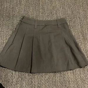 Grå kjol från H&M - Säljer en snygg grå kjol från H&M i storlek XXS. Kjolen har en klassisk design med veck framtill och hällor för bälte. Perfekt för både vardag och fest!