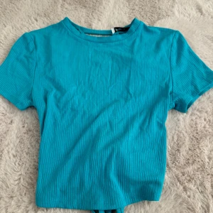 Blå t-shirt med öppen rygg  - Säljer denna fina t-shirt i en fantastisk blå färg. Aldrig använd. Sitter väldigt fint och har en knytning bak på ryggen. 