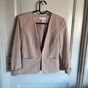 Rosa kavaj från H&M - Snygg rosa kavaj från H&M i storlek 36. Tillverkad i polyester och viskos med en touch av elastan för extra komfort. Kavajen har en stilren design med långa ärmar och en öppen front.