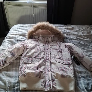 Ny vinterjacka med pälsdetaljer - Säljer en rutig vinterjacka med avtagbar pälskrage. Jackan har en dragkedja och knappar framtill samt praktiska fickor med lock. Jackan är ny med prislapp kvar.