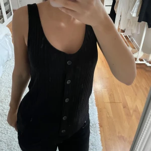 Svart ribbad linnetopp med knappar - Snygg svart ribbad linnetopp med knappar framtill. Perfekt för en stilren look. Passar bra till både jeans och kjol.