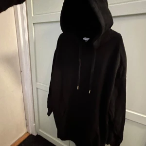 Svart hoodieklänning från H&M - Säljer en svart hoodieklänning, oversize, från H&M Basics. Den har en rymlig huva med dragsko och långa ärmar.
