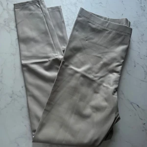 Beige skinn leggings  - Snygga beige leggings i skinn imitation med en elegant och stilren design. Perfekta för en chic och avslappnad look. De har en smickrande passform och är tillverkade i ett mjukt och bekvämt material. Långa ben med hög midja.