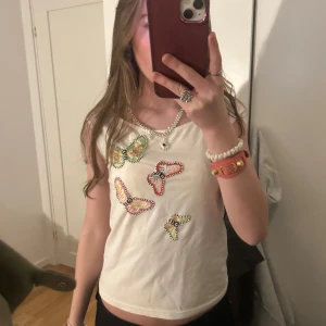 Vit linne med fjärilar - Säljer ett vitt linne med färgglada fjärilar på framsidan. Linnet har en enkel och stilren design med ärmlös passform. Perfekt för en somrig look! 🦋