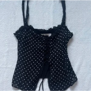 Svart prickig topp från Zara - Säljer en svart prickig topp från Zara med smala axelband och snörning framtill. Toppen har en söt volangdetalj vid halsringningen och är en jätte fin topp