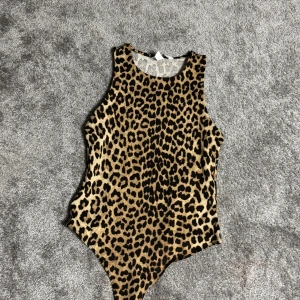 Leopardmönstrad ärmlös bodysuit - Snygg leopardmönstrad bodysuit i ett stretchigt material. Den är ärmlös och har en rund halsringning, perfekt för att lägga till en djärv touch till din outfit.