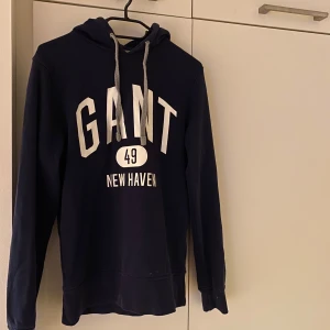 Mörkblå hoodie från GANT - Säljer en snygg mörkblå hoodie från gant i storlek XS men passar även S och justerbar huva med snören. Perfekt för en avslappnad stil.