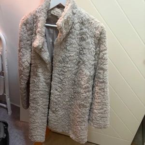 Beige teddyjacka  - Mysig beige teddyjacka. Perfekt för kyliga dagar med sin fluffiga och varma design. Jackan har en klassisk krage och långa ärmar.