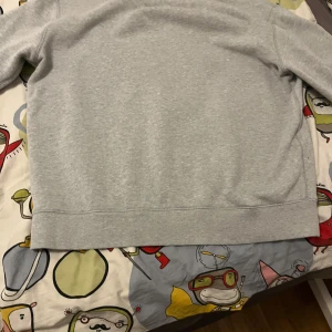Grå sweatshirt från Ralph Lauren - Säljer en stilren grå sweatshirt från Ralph Lauren med en liten broderad logga på bröstet. Tröjan har långa ärmar och en klassisk passform. Perfekt för en avslappnad look.