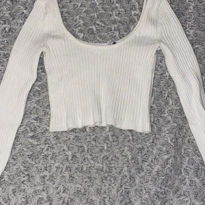 Vit ribbad croppad topp från Bershka - Säljer en stilren vit ribbad topp från Bershka. Den är croppad med långa ärmar och en rundad halsringning. Perfekt för en trendig look!