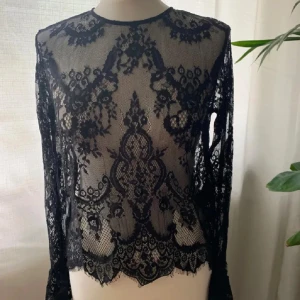 Svart spetsblus - Elegant svart spetsblus med intrikata blommönster. Blusen har långa ärmar och en rund halsringning. Perfekt för en stilfull look. Lånade bilder (kan även skicka hur den sitter på mig) 